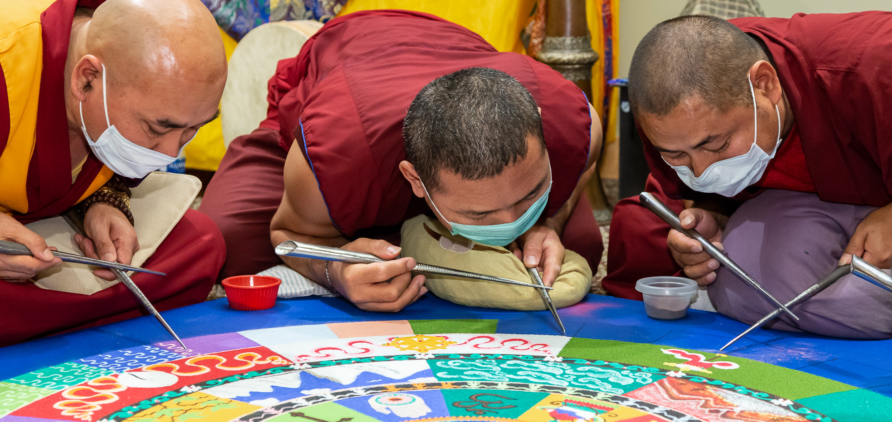 The monks rapidly rub their chak-purs together to deposit sand onto the mandala surface. They also wear masks over their mouths to avoid blowing the sand with their breath. (DePaul University/Jeff Carrion)